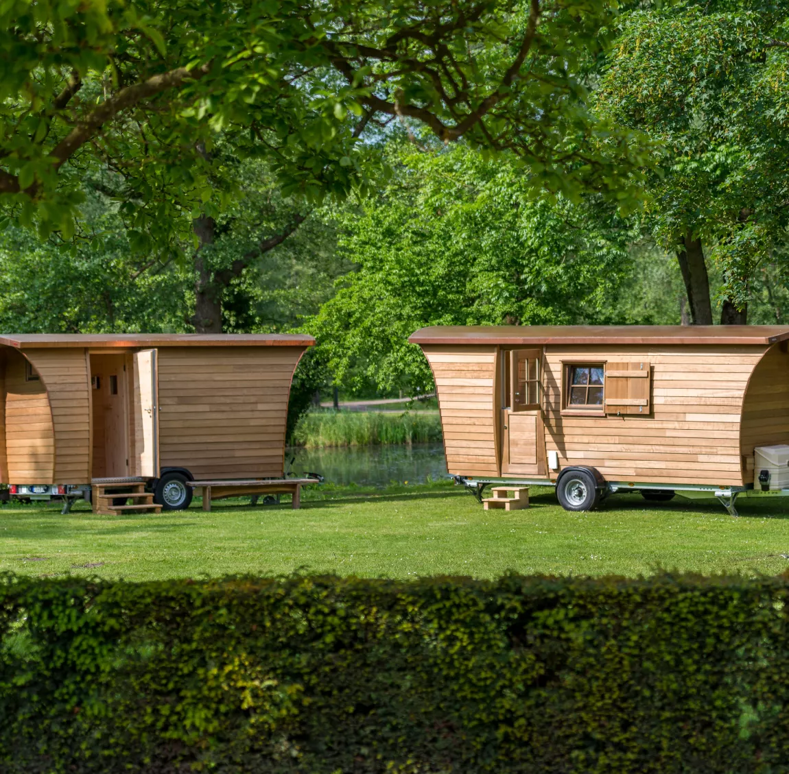Zwei Tannhäuschen als mobile Sauna und fahrbarer Wohnwagen auf grüner Wiese im Sommer